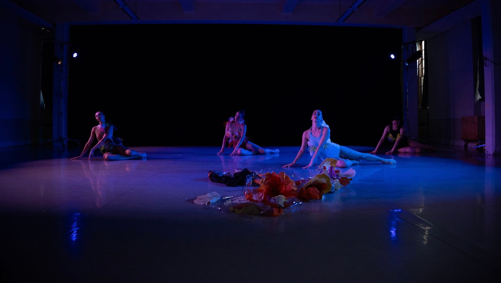 Four dancers on the floor of a dark room gazing upwards