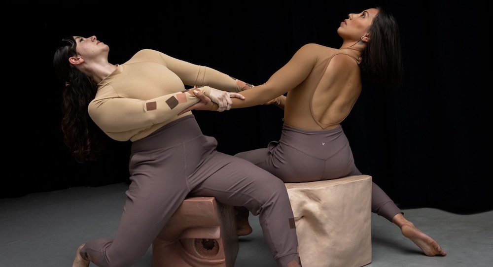 Two figures grasping each other's arms and leaning back against a black backgrou
