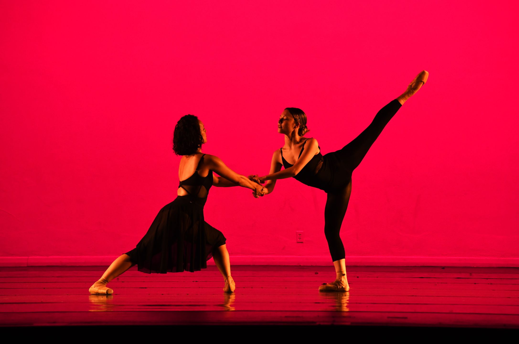 2 ballet dancers are posed on stage with a hot pink backdrop and a shiny black f