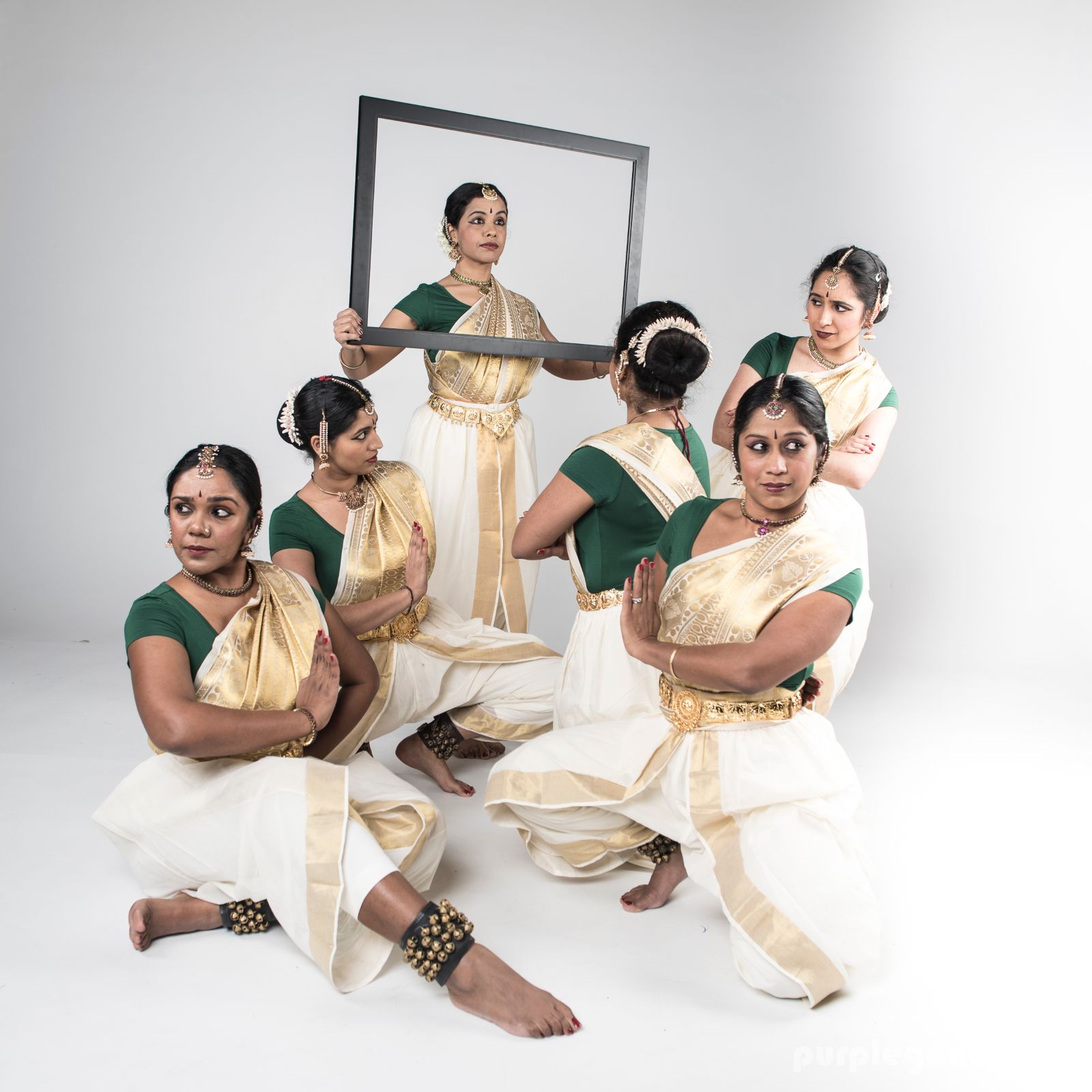 Six women in traditional Indian clothes squat while facing different directions.
