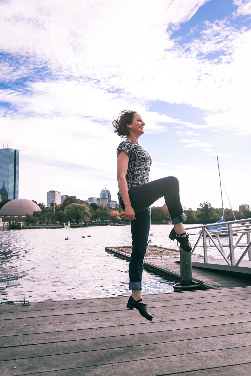 Woman jumping with one leg straight and the other bent in front of a dock