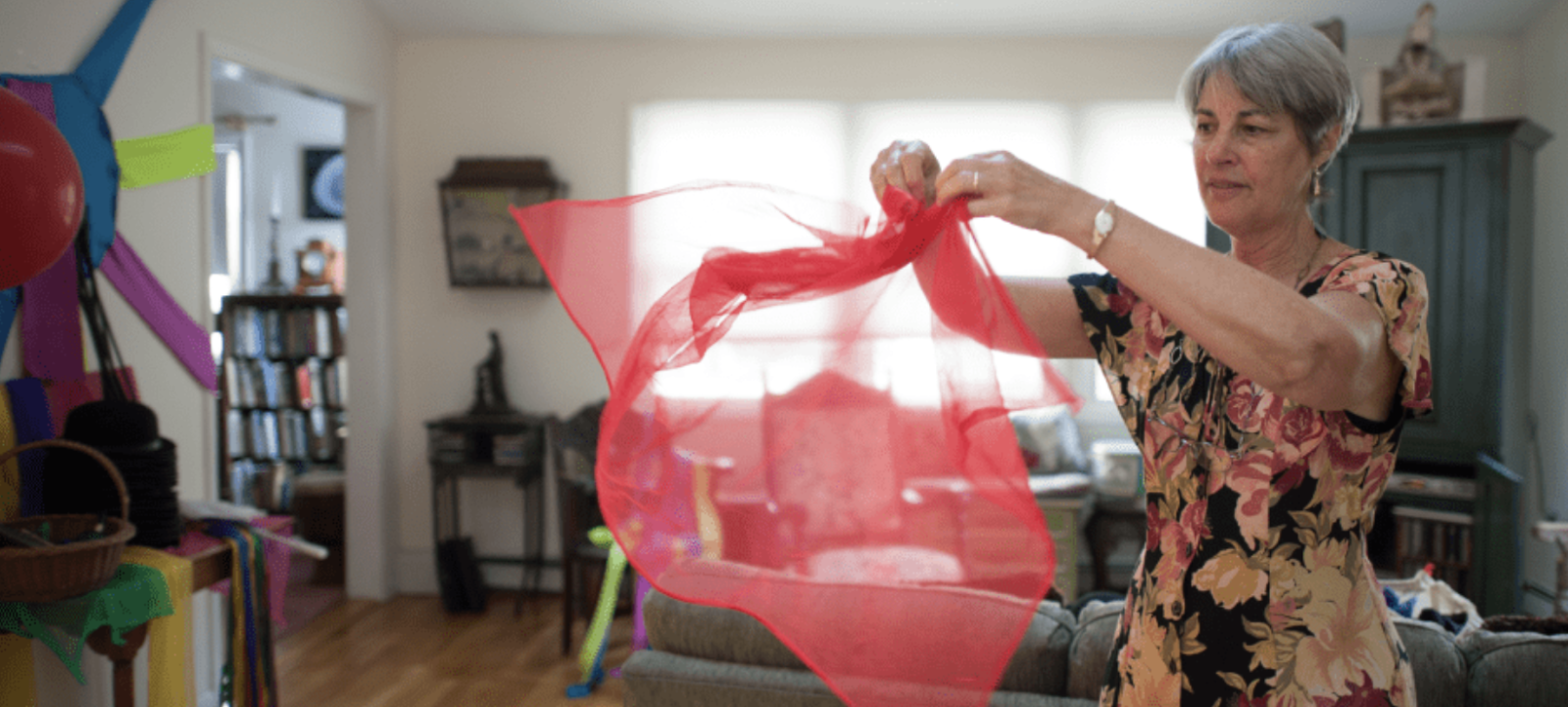 Woman with gray hair spinning a transparent red cloth in a living room