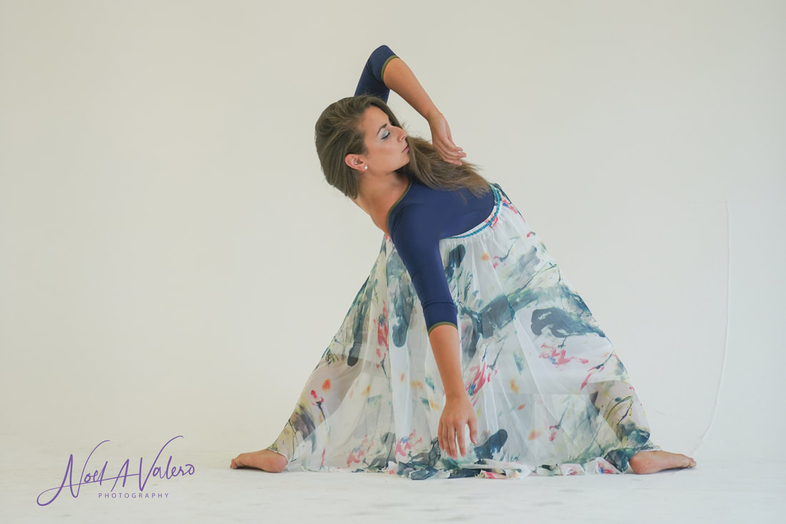 Woman in blue blouse and light colored skirt bending down with one arm extending