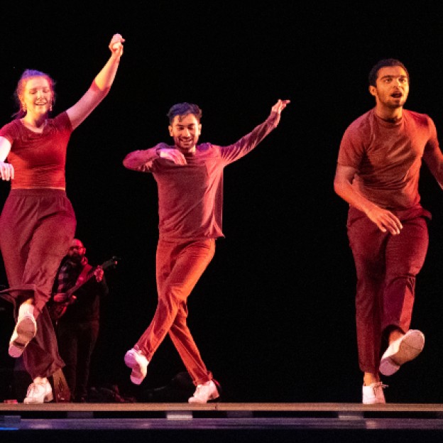 Three tap dancers in red lighting mid-tap