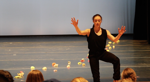 Performer in black holding up her hands with a string of yellow objects on the f